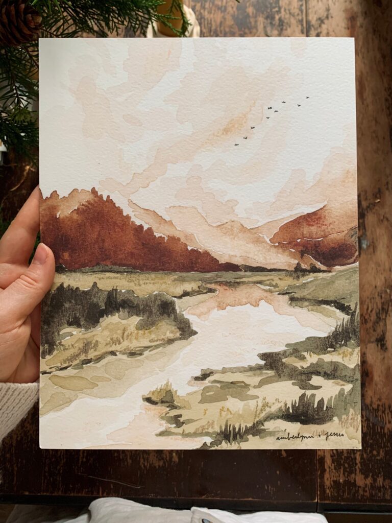 a hand holding a painting of a river