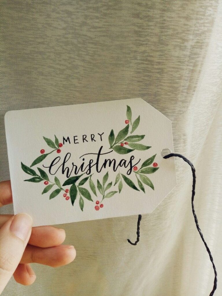 A person holding up a christmas gift tag with the words merry christmas.