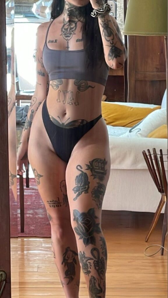 A woman in a bikini with tattoos taking a selfie.