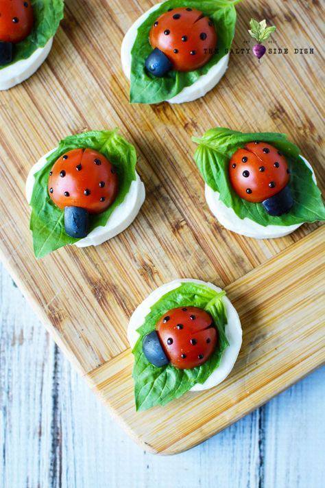 Ladybug appetizers with olives and tomatoes on a cutting board.