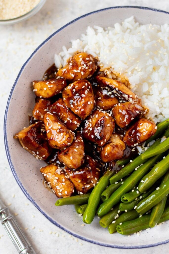 A bowl of asian chicken with green beans and rice.