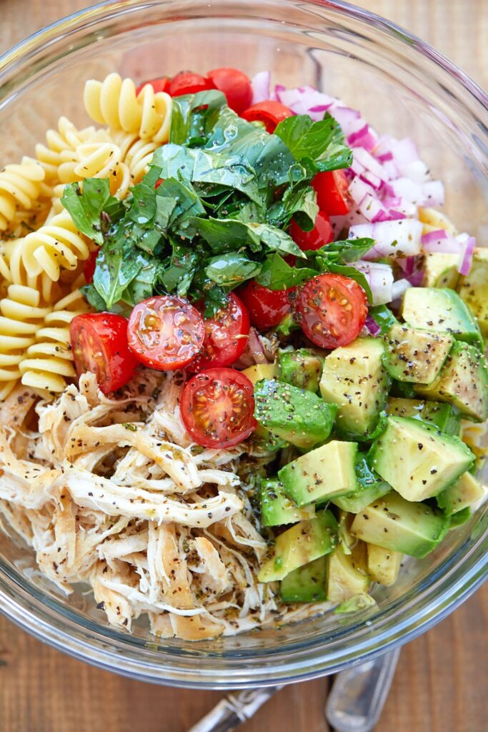 A bowl of pasta salad with chicken, tomatoes and avocado.