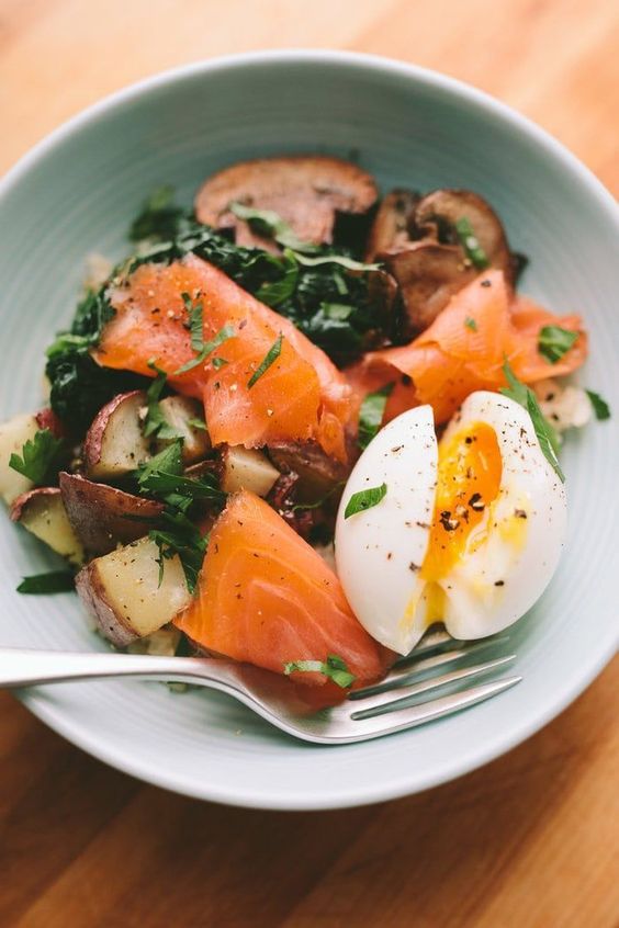 A bowl of smoked salmon, kale, potatoes and a hard boiled egg.