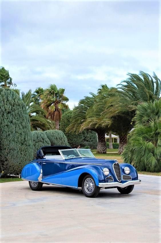 A blue vintage car parked in front of a palm tree.