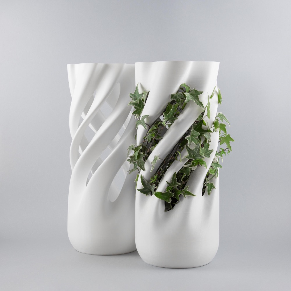 Two white, wavy ceramic vases with ivy plants spilling out, set against a plain grey background.