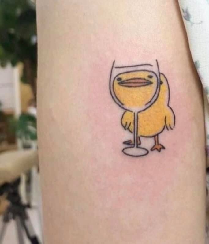 A tattoo on a person's arm depicting a cartoon character with the body of a bird and the head of a wine glass.