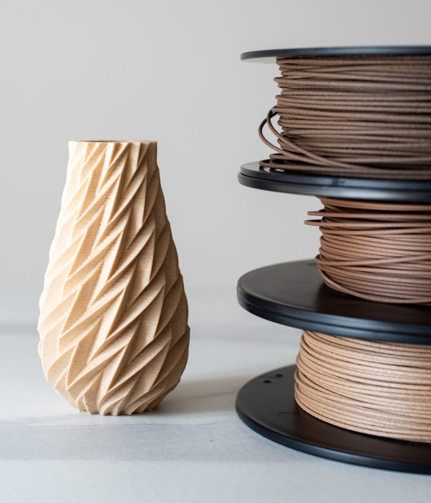 A 3d-printed vase with a geometric pattern next to spools of brown filament on a gray background.
