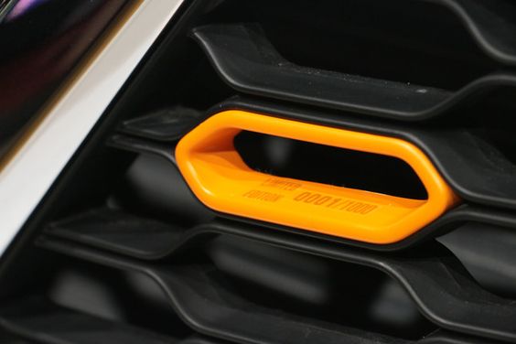 Close-up of a vibrant orange tow hook on a black car grille, with visible text on the hook reading "1000 kg.
