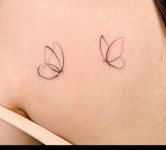 Two minimalist butterfly tattoos on a person's back, drawn with fine black lines.