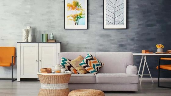Modern living room with a gray sofa, colorful cushions, a woven ottoman, and decorative wall art.