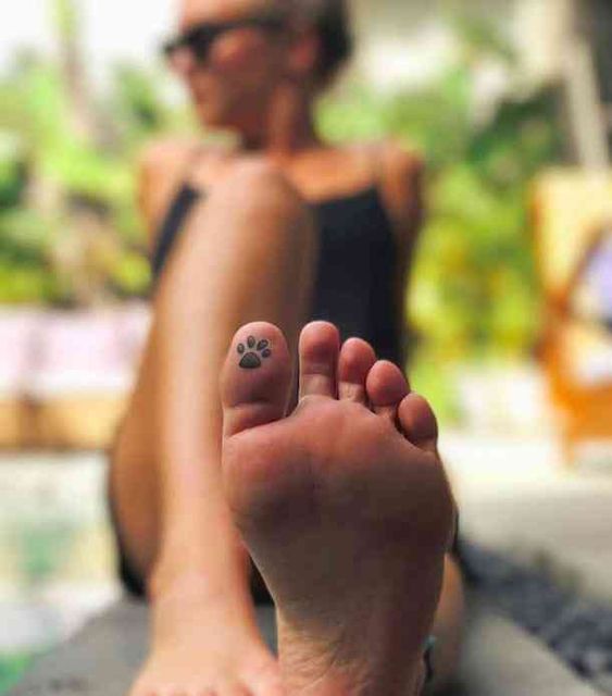 Woman relaxing in a chair with her foot foregrounded, showing a tattoo of a paw print on her big toe.