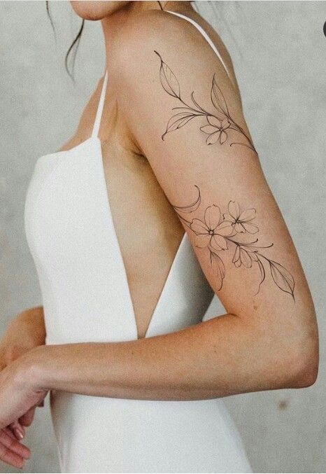 A woman in a white dress, showing a delicate floral tattoo on her upper arm.