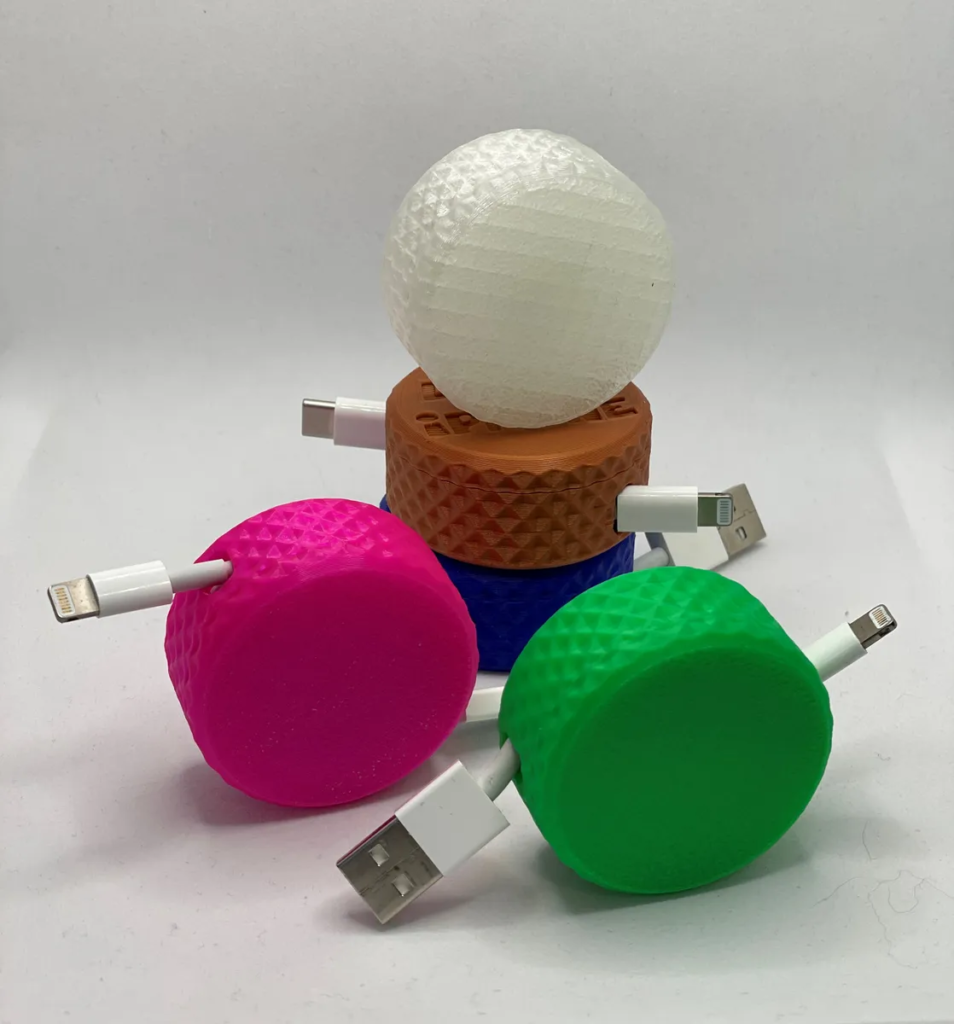 Five colorful spherical usb chargers with cords, stacked and arranged in a pyramid shape on a plain background.