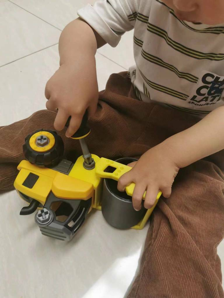 A child plays with a yellow toy construction vehicle on a tiled floor.
