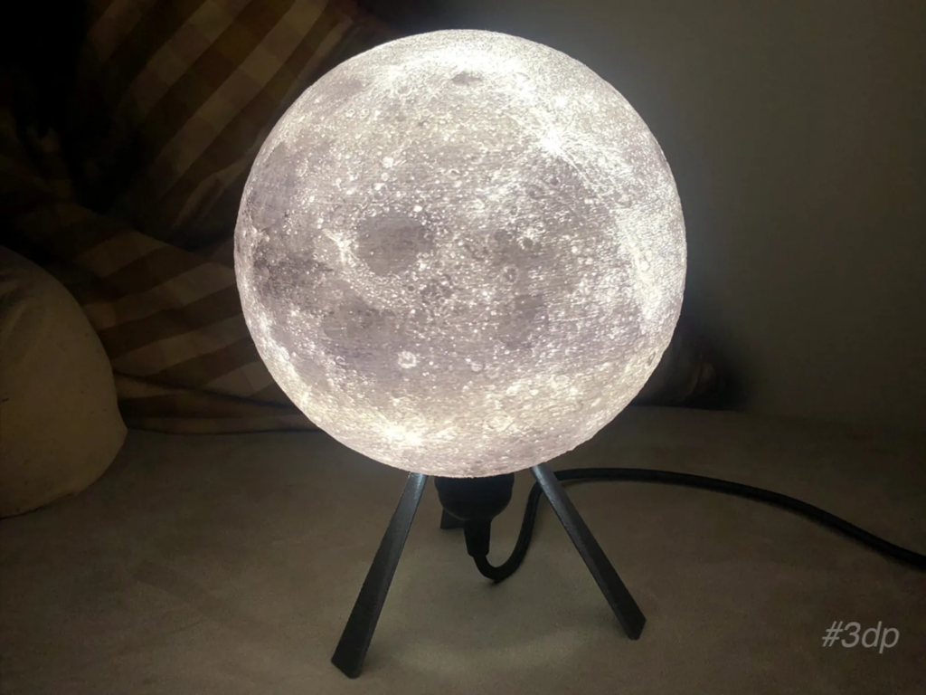 A glowing moon lamp on a stand, illuminated against a dark background, displaying detailed lunar surface features.