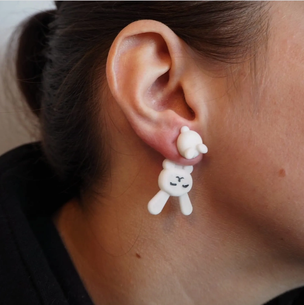 Close-up of a woman's ear wearing a white earring shaped like a cute character with a smiling face.