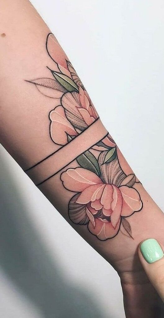 Forearm tattoo featuring pink flowers and green leaves, intersected by two black horizontal lines. Mint green nail polish on the thumb is visible holding the arm.