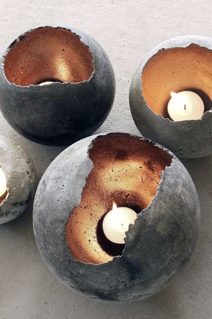 Four round concrete candle holders with rough edges and a golden interior finish, each holding a lit white tealight candle.