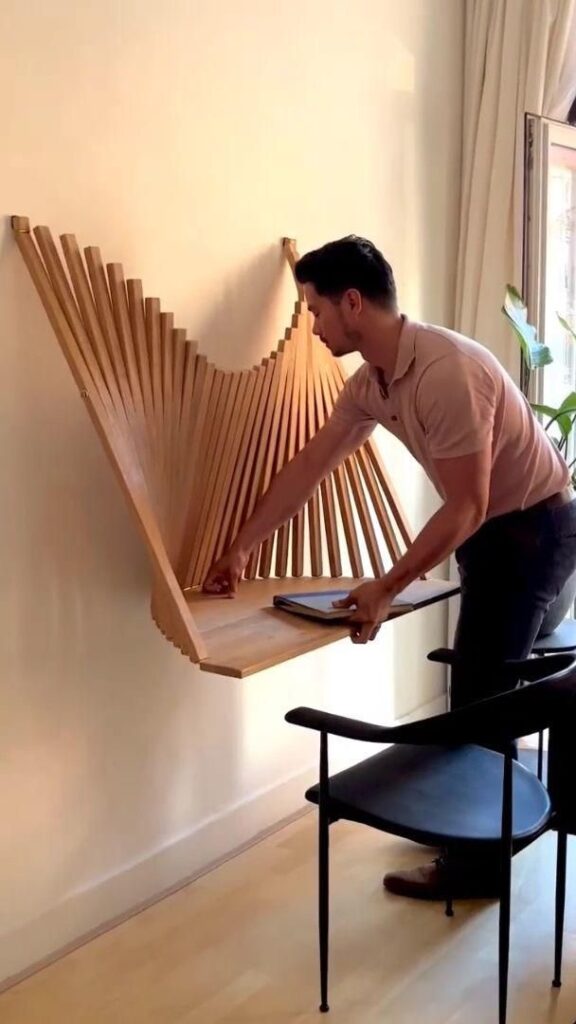 A person unfolds a wooden wall-mounted desk while placing a book or laptop on its surface in a well-lit room.