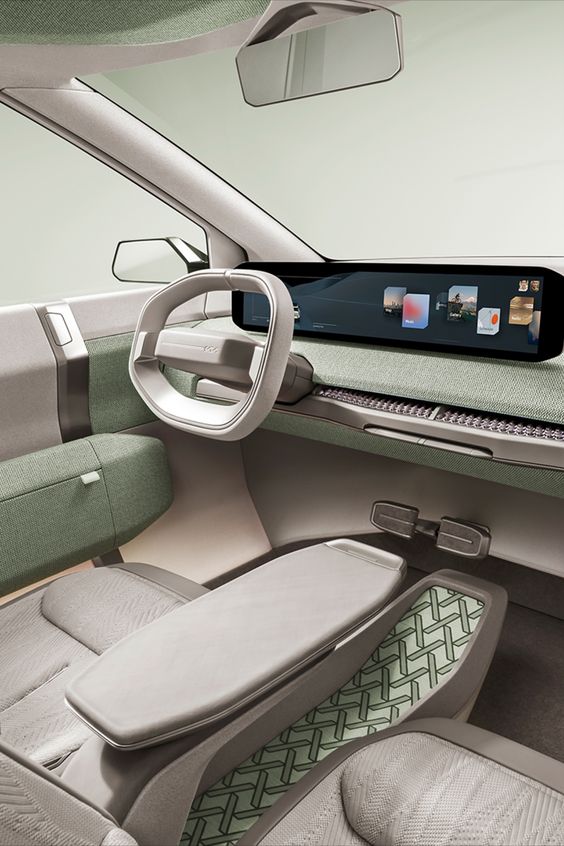 Futuristic car interior with a minimalist design. Features a large digital dashboard display, sleek steering wheel, light gray and green seats, and matching dashboard.