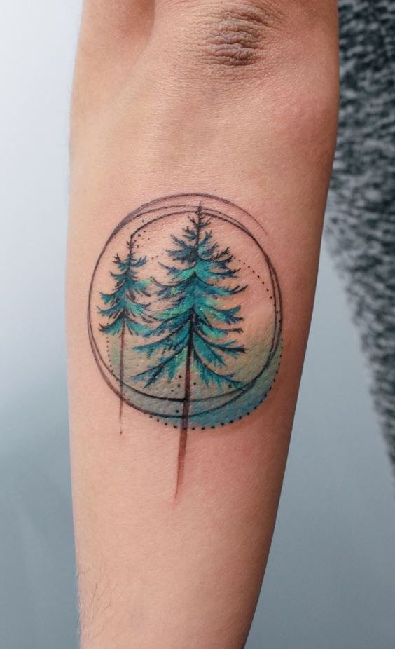 A tattoo of two evergreen trees with a circular geometric design, enclosed within faint dotted lines, located on a person's forearm.