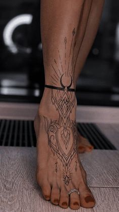 A foot with intricate black, geometric and celestial-themed tattoos extending from the toes to the ankle, standing on a wooden floor.