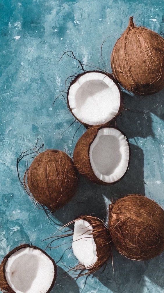 Six brown coconuts, some whole and some split open, are scattered on a blue textured surface.