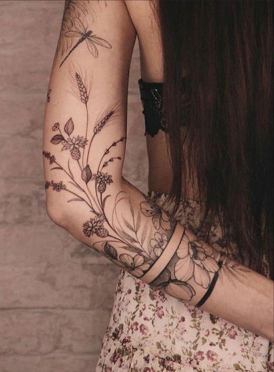A person with long hair and floral tattoos on their arm is wearing a floral skirt and a black top.