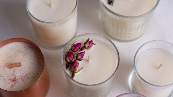 Assorted scented candles with decorative elements like rose petals and cinnamon, displayed on a light fabric surface.