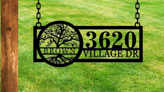 A hanging address sign featuring a tree design and the text "3620 brown village dr" against a grassy background.