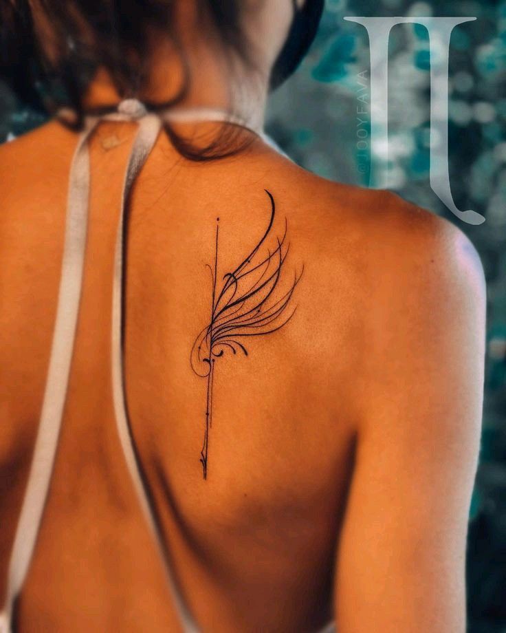 Close-up of a woman's upper back showing a delicate wing tattoo. The woman is wearing a halter top, and the background is blurred greenery.