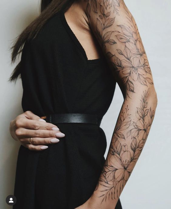 A person in a black dress displays a detailed floral tattoo sleeve on their left arm.