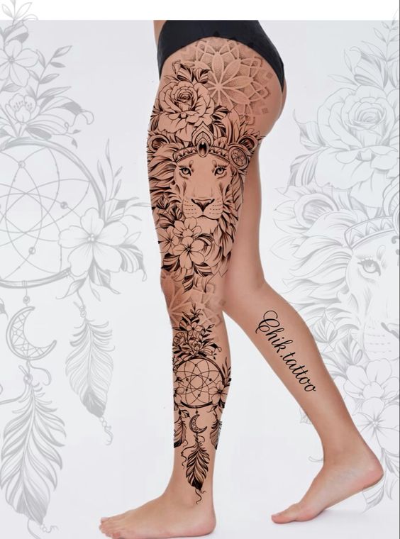 A person's leg tattoo featuring an intricate lion's face adorned with flowers, feathers, and other ornamental designs extending from the thigh to the ankle.