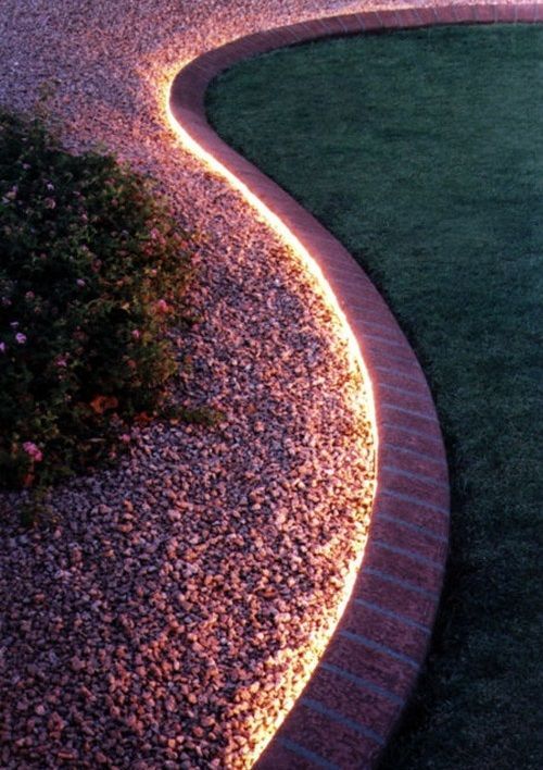 Curved landscape featuring a gravel path, brick border, and illuminated edge separating the gravel from a grass-covered area.