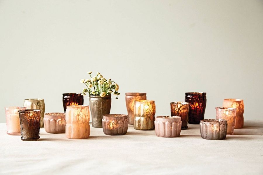 Assorted candle holders in various shades and textures, some illuminated, on a plain backdrop with subtle shadows.