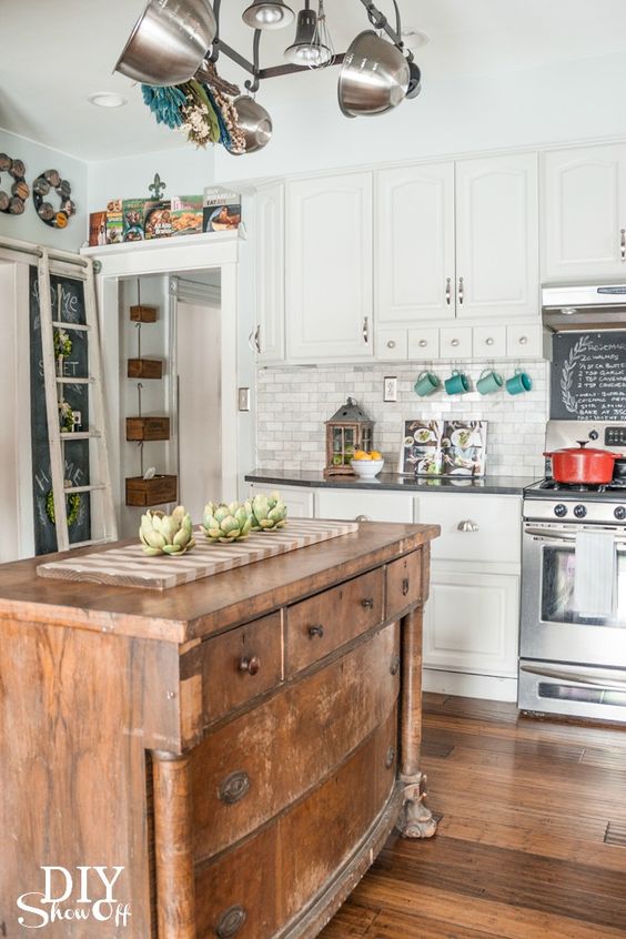 Vintage farmhouse kitchen with wooden island, white cabinets, modern lighting, and rustic decor elements.