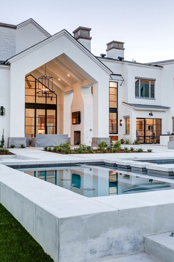 Modern white house exterior with large windows, spacious patio, and luxury pool reflecting the architectural design.