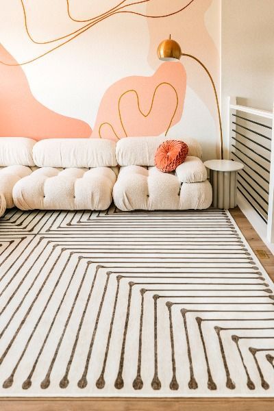 Modern living room with abstract mural, comfy white sofa, geometric patterned rug, and gold floor lamp.