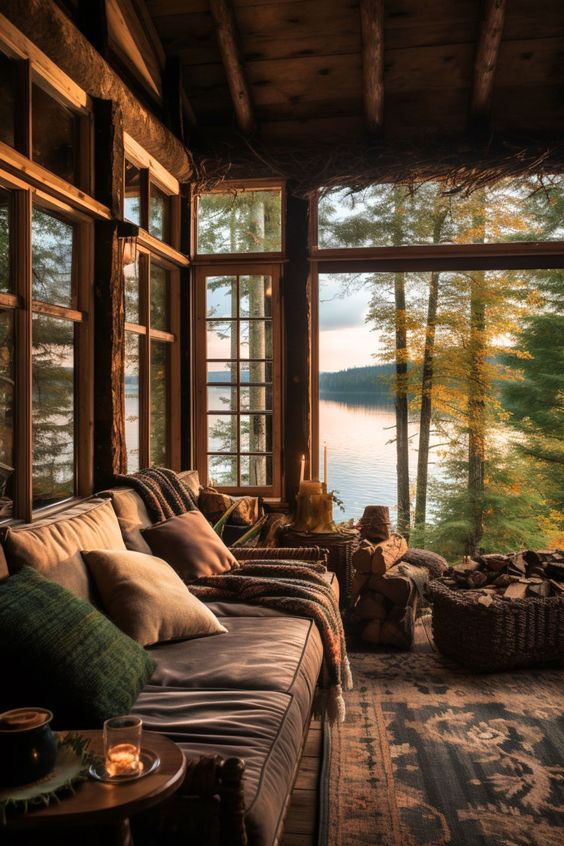 Cozy lakeside cabin interior with rustic decor, comfy sofa, and large windows framing a serene sunset over the lake.