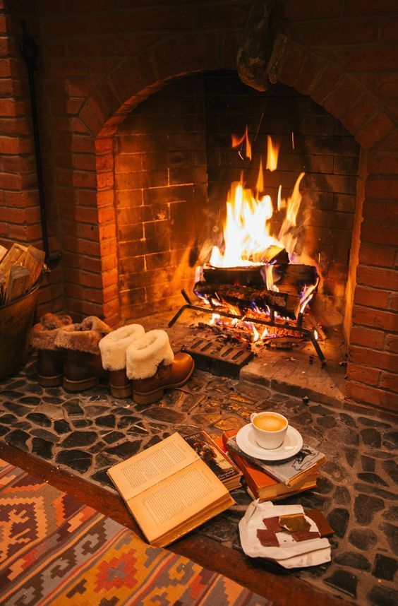 Cozy fireplace scene with burning wood, books, hot beverage, and warm boots, perfect for relaxing winter evenings.
