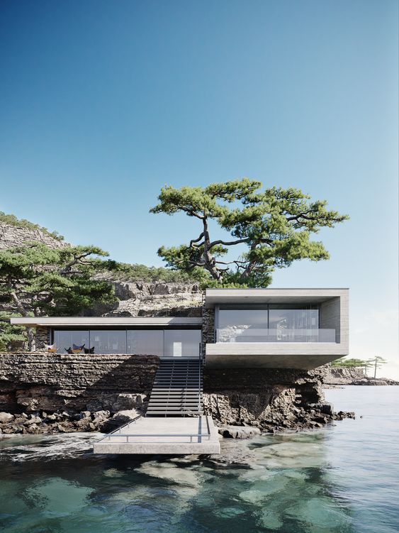 Modern house with large glass windows situated on a rocky cliff by the water, featuring an exterior staircase and a large tree growing from the roof.
