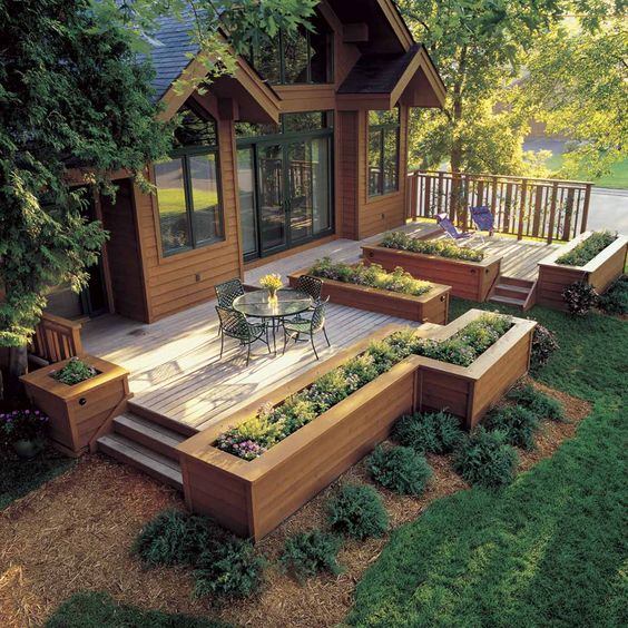 Modern wood deck with elevated garden beds and outdoor seating, surrounded by lush greenery and trees.