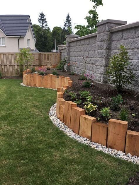 Beautiful backyard garden with raised wooden planters along stone wall, featuring blooming flowers and green plants.