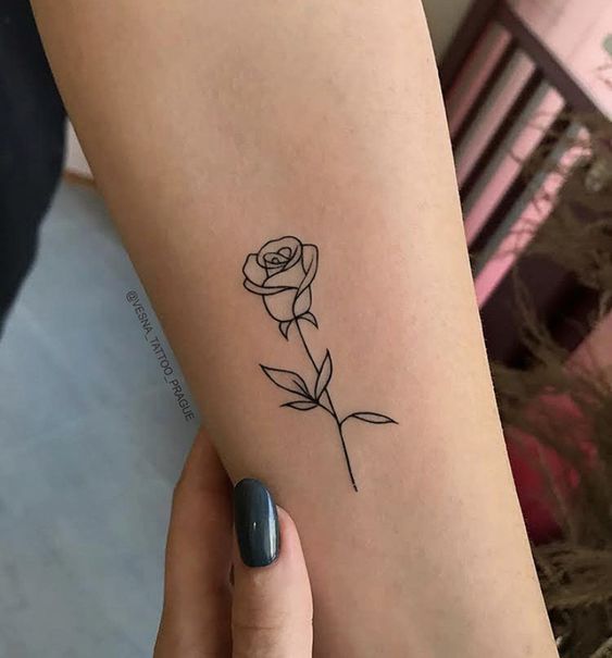 Minimalist single-line rose tattoo on a forearm, held by a hand with dark nails, showcasing elegant body art.
