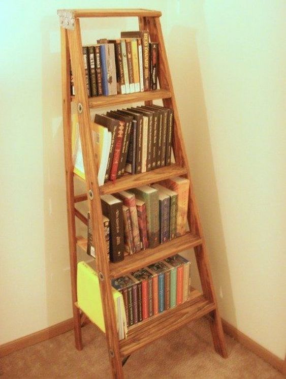 Rustic wooden ladder repurposed into a bookshelf, filled with various books in a cozy corner of a room with beige walls.