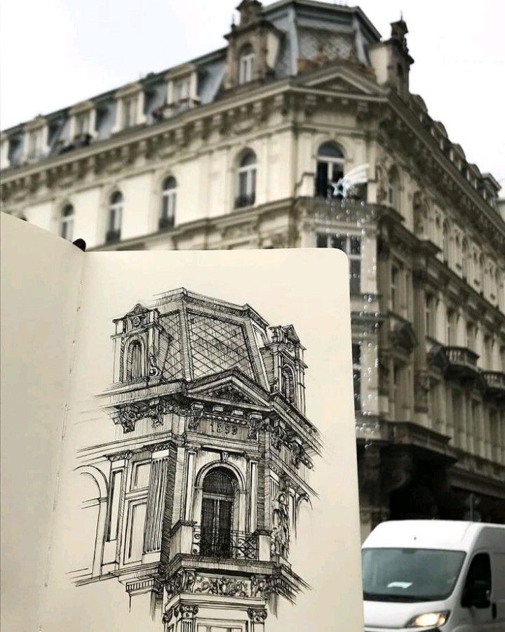 A sketch of a detailed building facade is held in front of the same architectural building, with a white van passing by in the background.