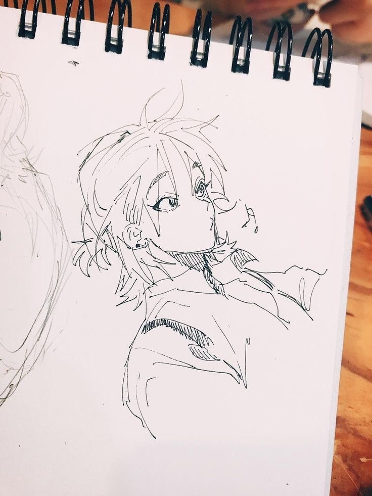 A sketch of an anime-style character with short, messy hair and wide eyes, drawn on a spiral-bound sketchpad.