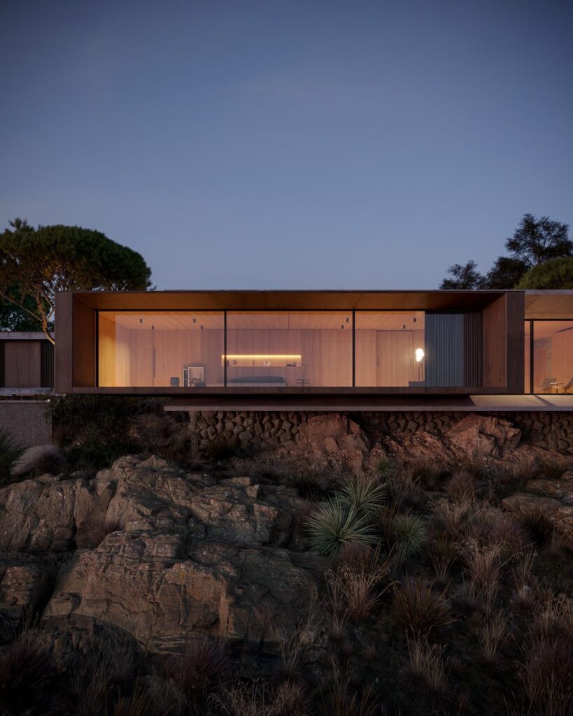 Modern home with large glass windows, illuminated interior, and minimalist design perched on a rocky hillside at dusk.