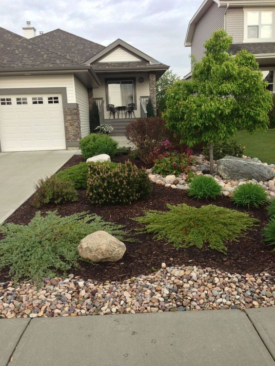 Modern front yard landscaping with various shrubs, rocks, and mulch in a suburban neighborhood, enhancing curb appeal.