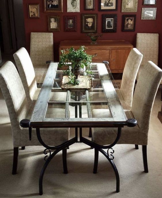 Elegant dining room with a glass top table, beige upholstered chairs, and vintage photo gallery wall. Indoor plants centerpiece.